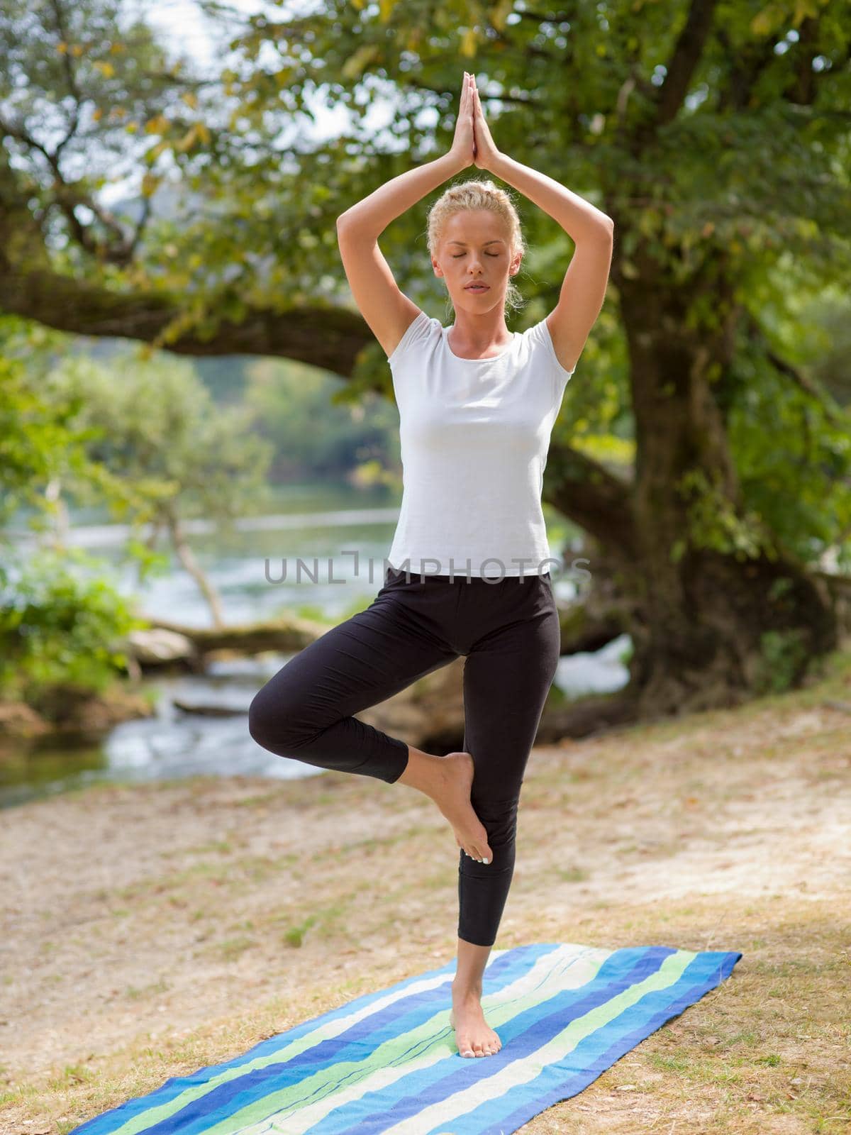 healthy woman relaxing while meditating and doing yoga exercise in the beautiful nature on the bank of the river