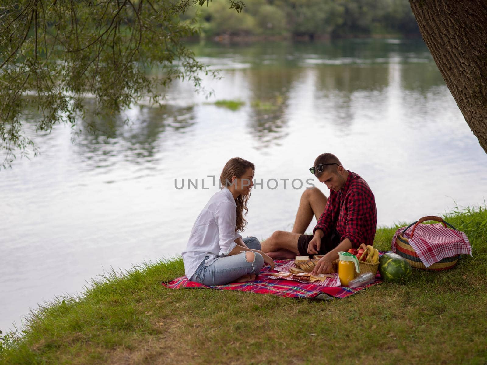 Couple in love enjoying picnic time drink and food in beautiful nature on the river bank