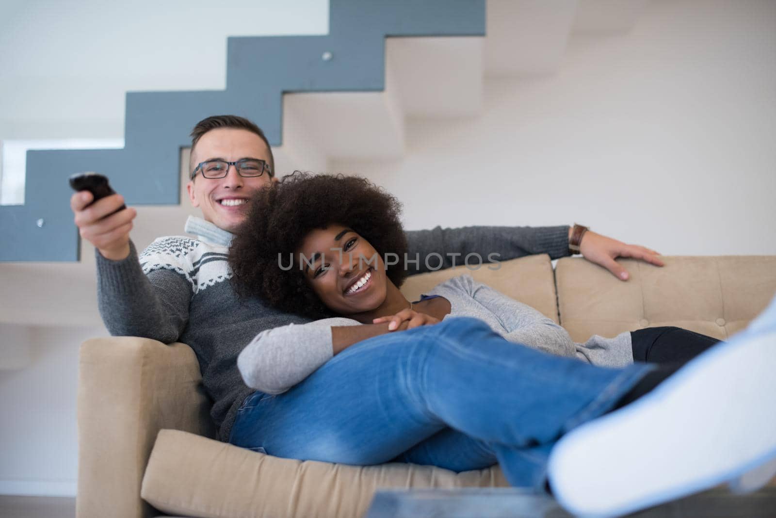 Young multiethnic couple relaxing on the sofa in the luxury living room, using a laptop and remote control