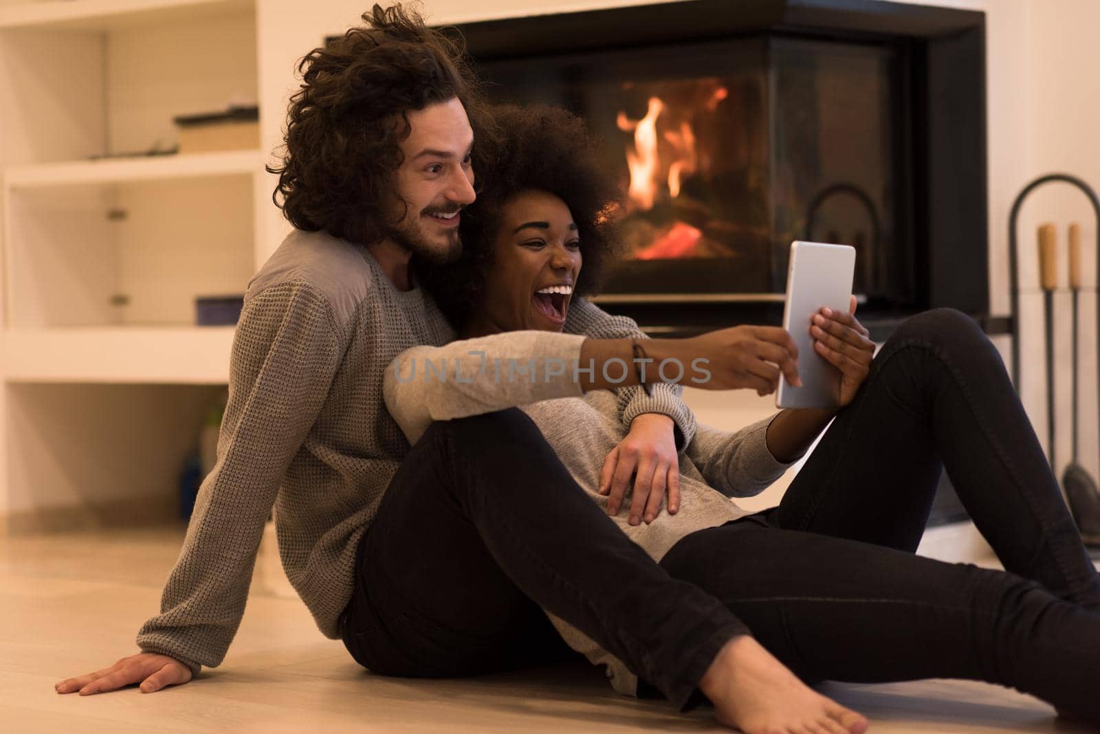 beautiful young multiethnic couple using tablet computer on the floor of their luxury home in front of fireplace at autumn day