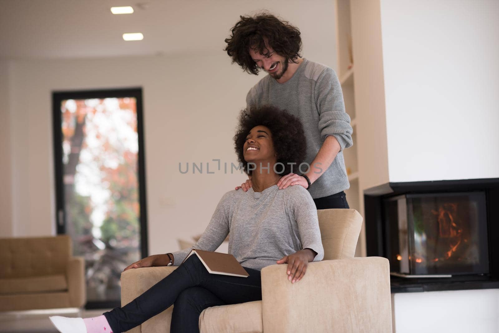 Young beautiful multiethnic couple hugging in front of fireplace at home when reading a book at autumn day