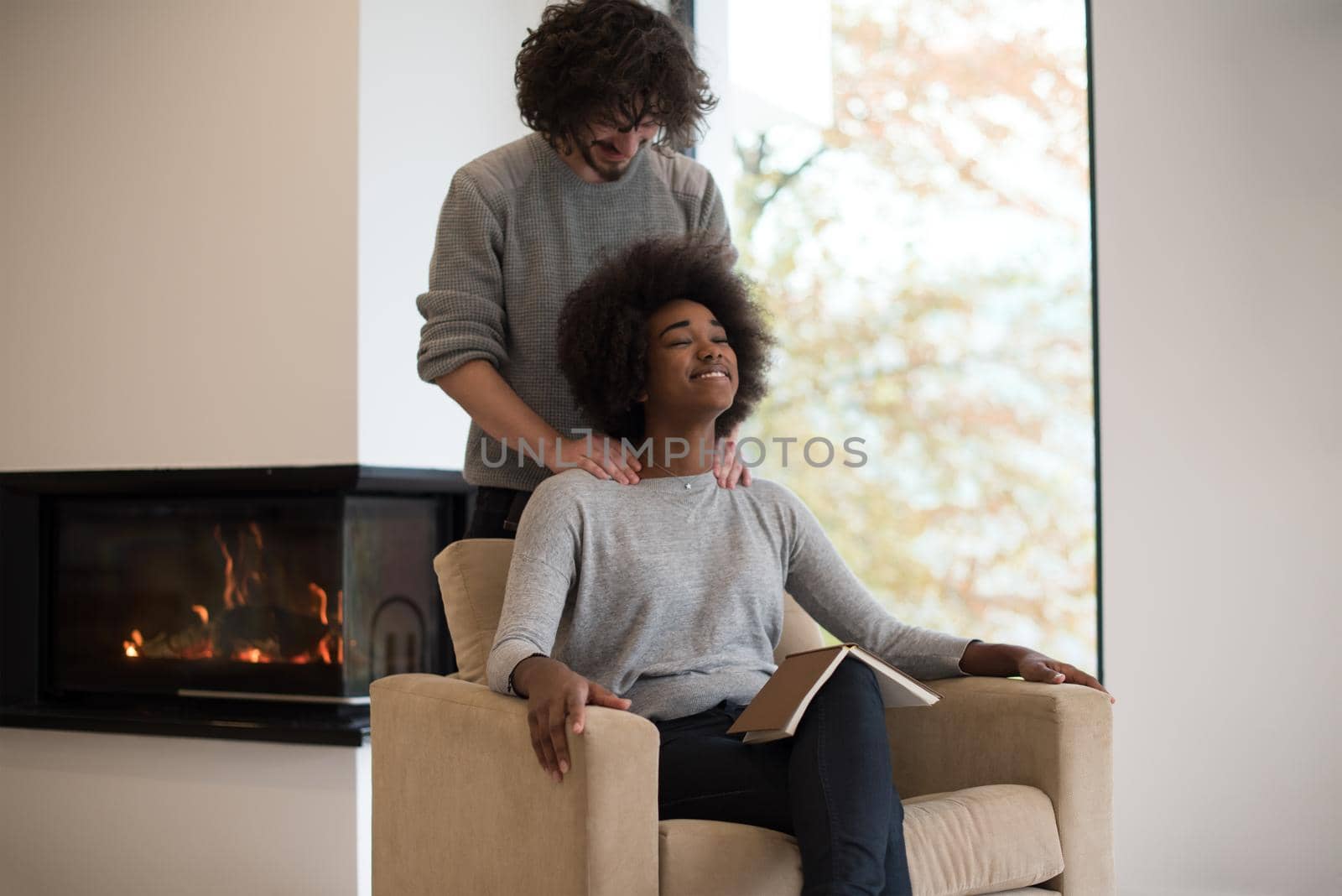 Young beautiful multiethnic couple hugging in front of fireplace at home when reading a book at autumn day