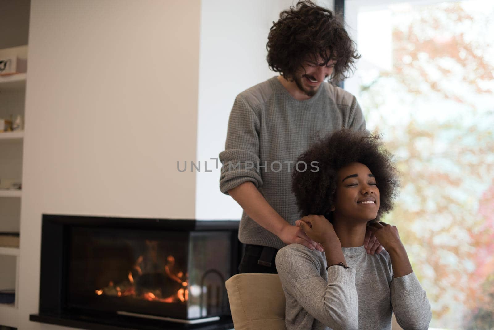 Young beautiful multiethnic couple hugging in front of fireplace at home when reading a book at autumn day