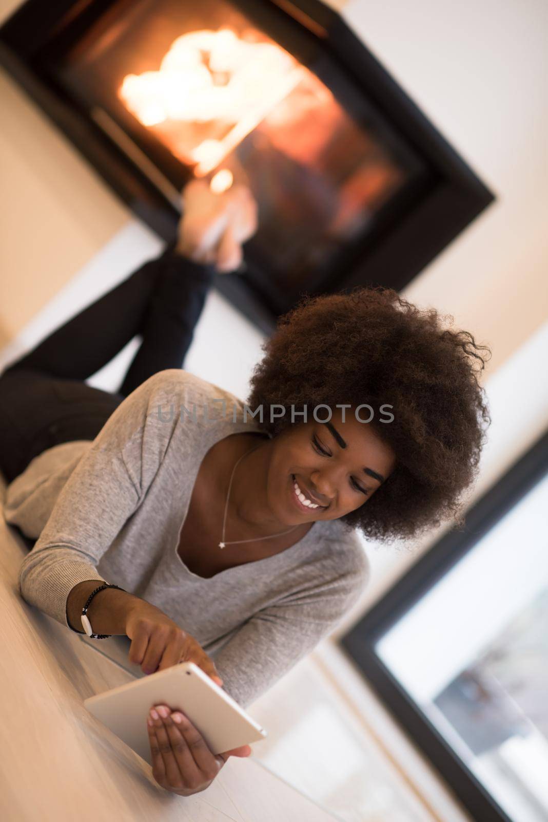 beautiful young black women using tablet computer on the floor of her luxury home in front of fireplace at autumn day