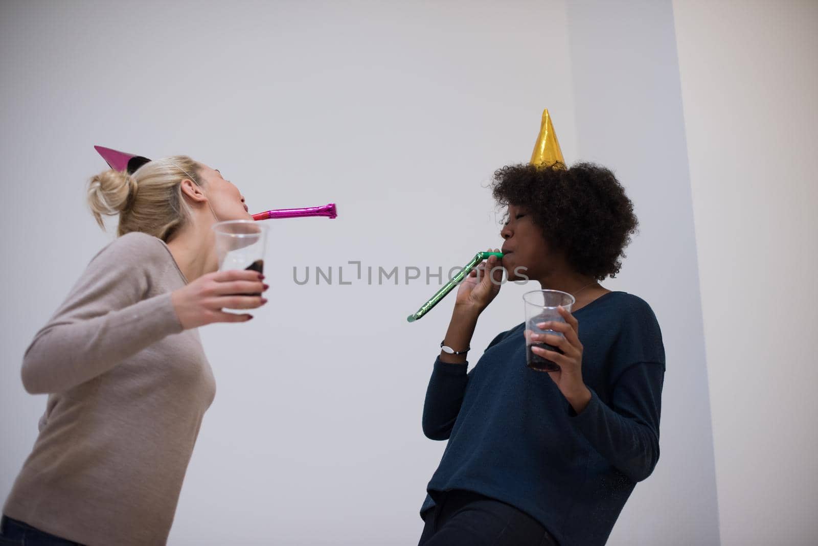 people and celebration concept  young multiethnics smiling women in party caps blowing to whistles