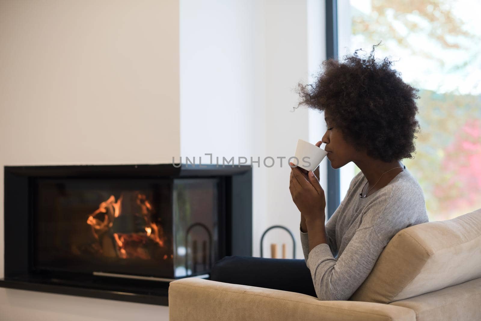 black woman drinking coffee in front of fireplace by dotshock
