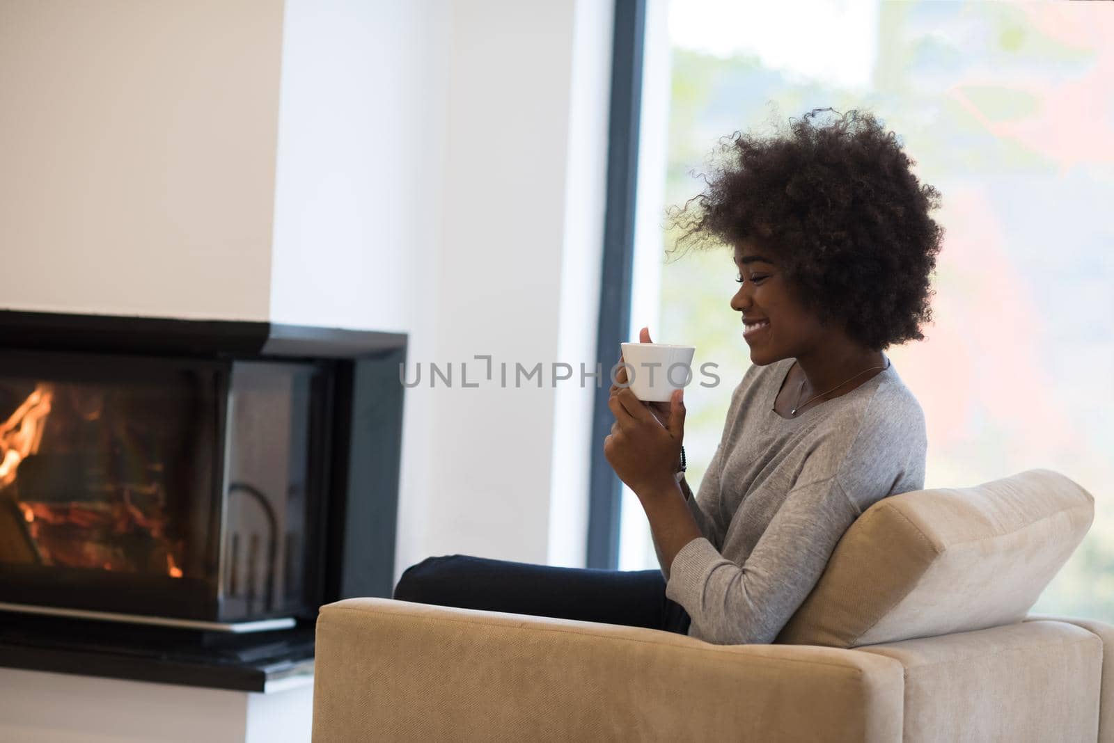 Happy joyful african american woman drinking cup of coffee relaxing at fireplace. Young black girl with hot beverage heating warming up. autumn at home.