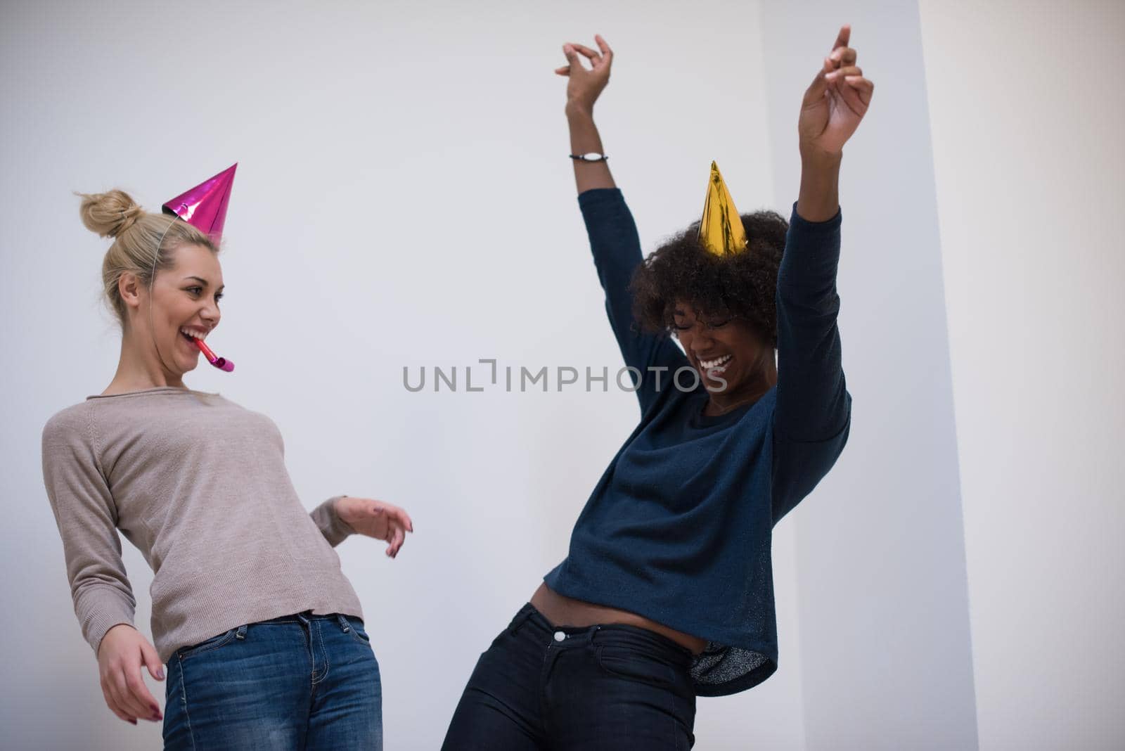 people and celebration concept  young multiethnics smiling women in party caps blowing to whistles