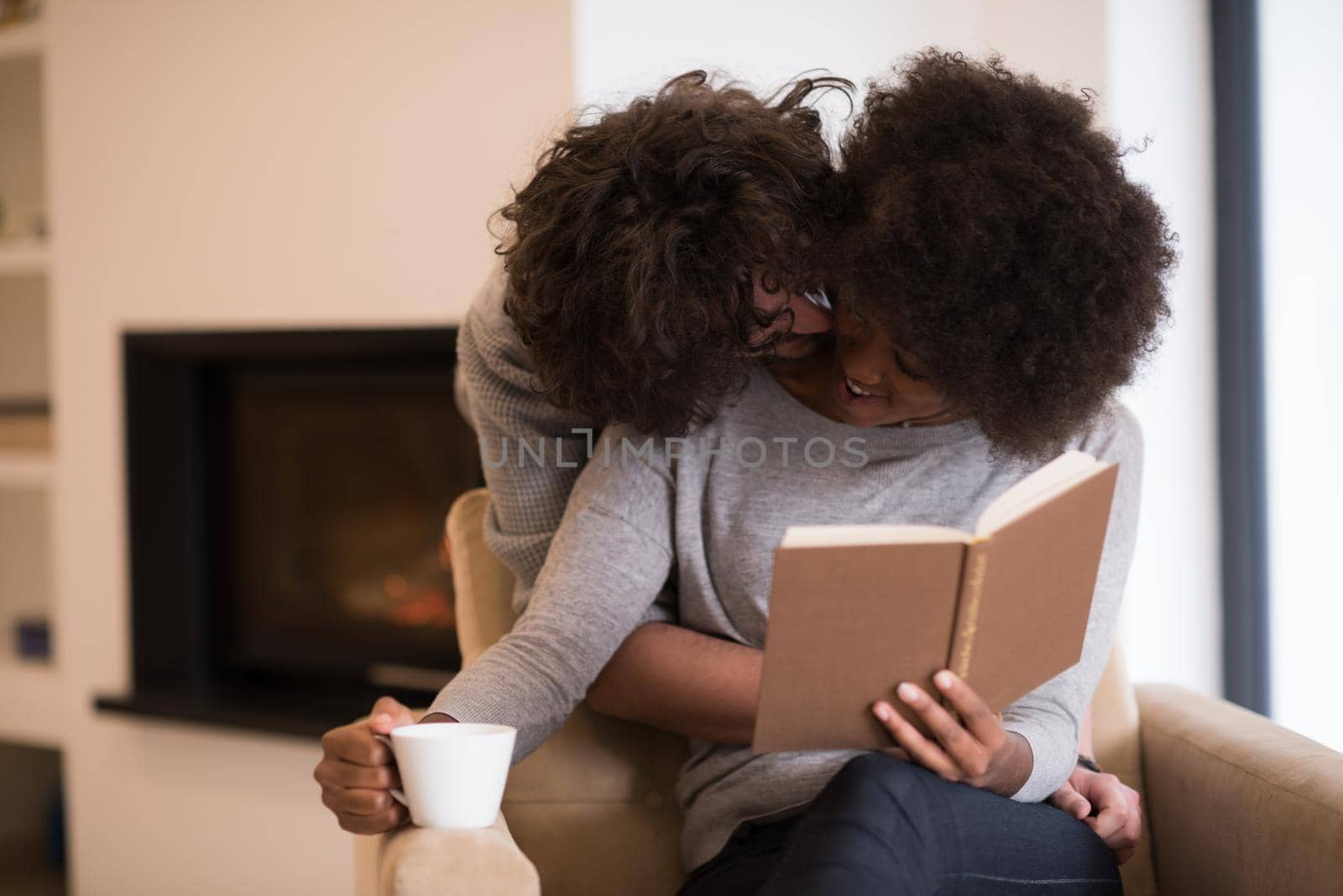 Young beautiful multiethnic couple hugging in front of fireplace at home when reading a book at autumn day