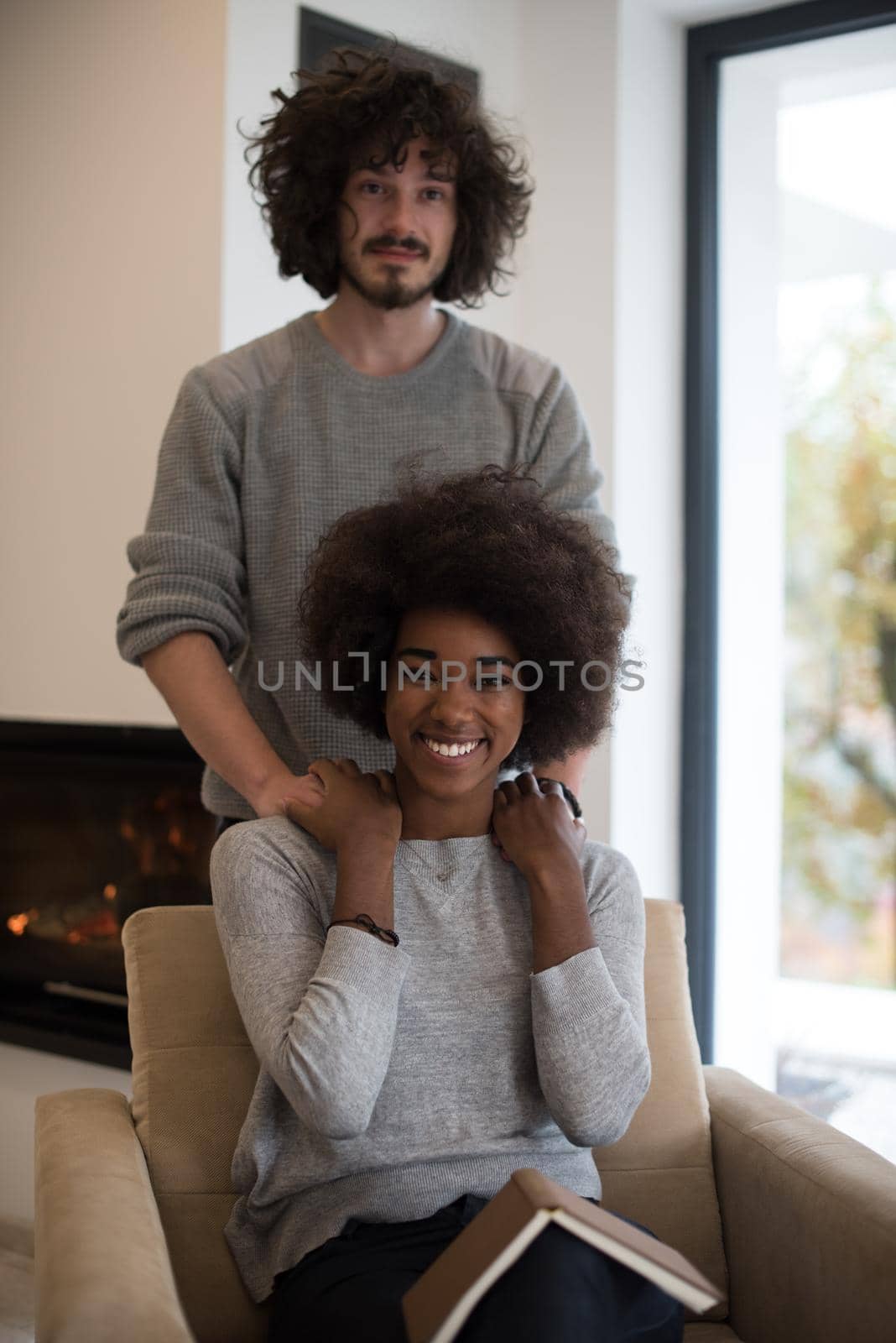 Young beautiful multiethnic couple hugging in front of fireplace at home when reading a book at autumn day