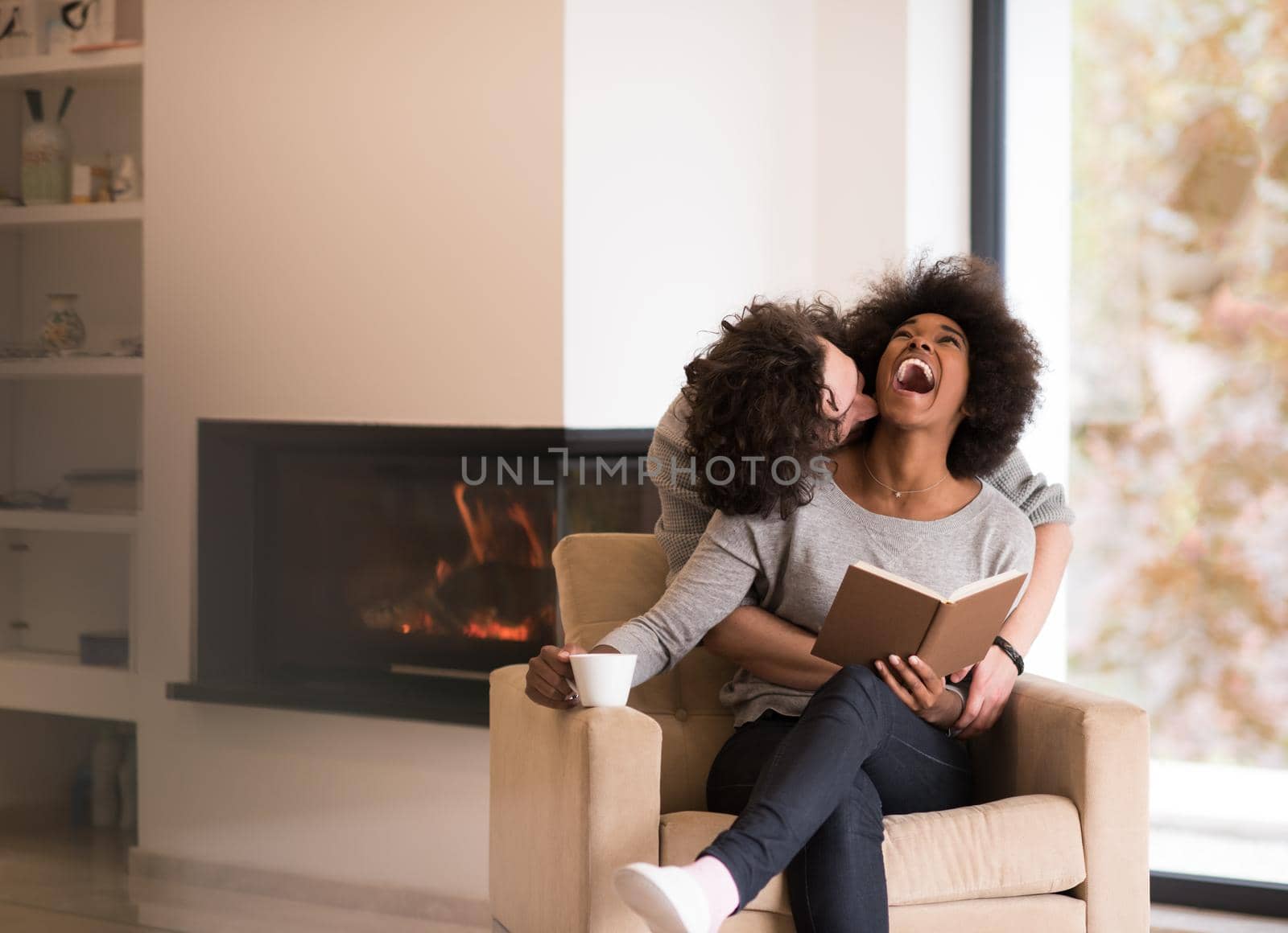 Young beautiful multiethnic couple hugging in front of fireplace at home when reading a book at autumn day