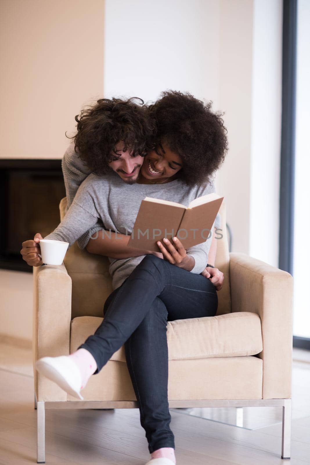 Young beautiful multiethnic couple hugging in front of fireplace at home when reading a book at autumn day