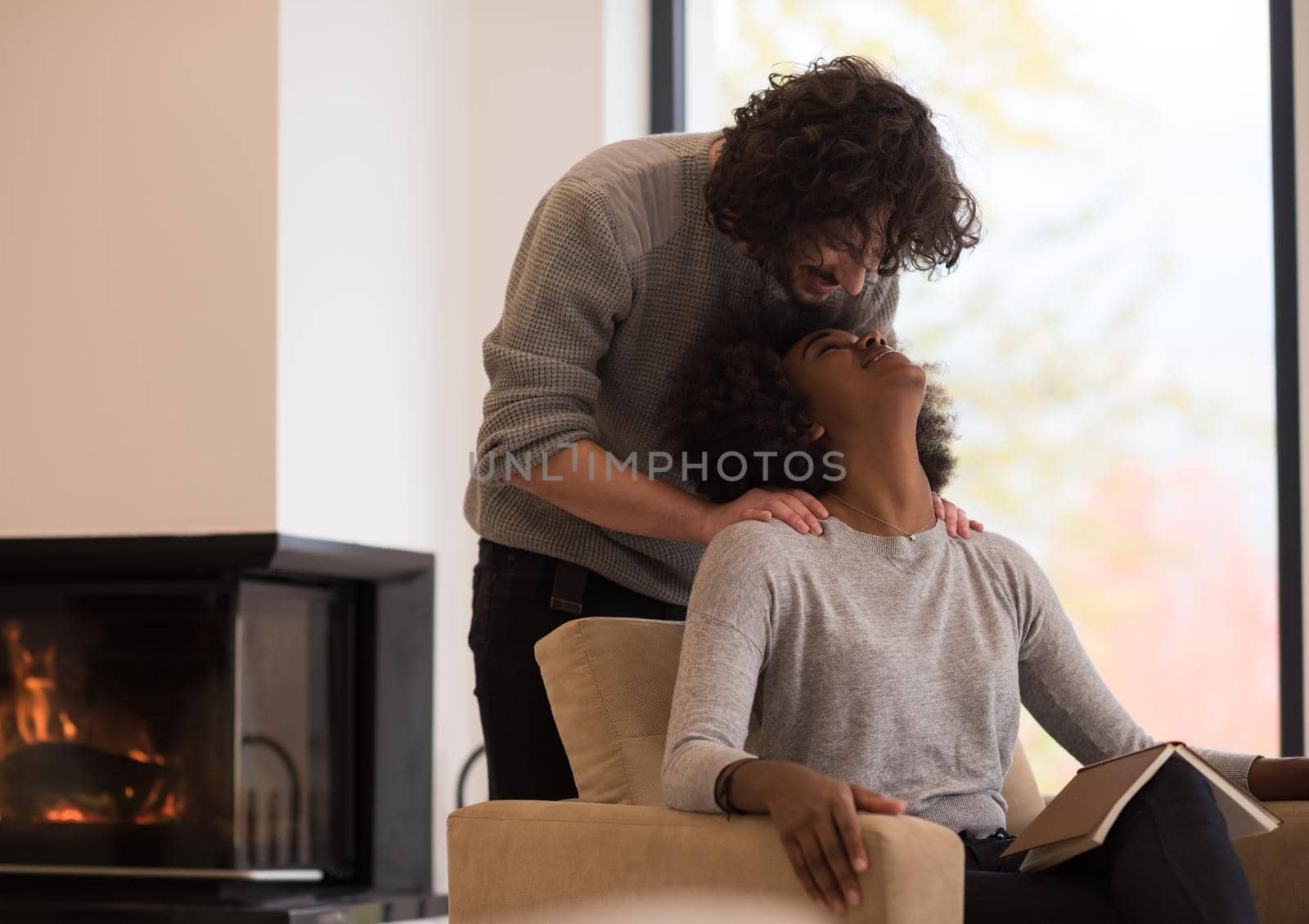 Young beautiful multiethnic couple hugging in front of fireplace at home when reading a book at autumn day