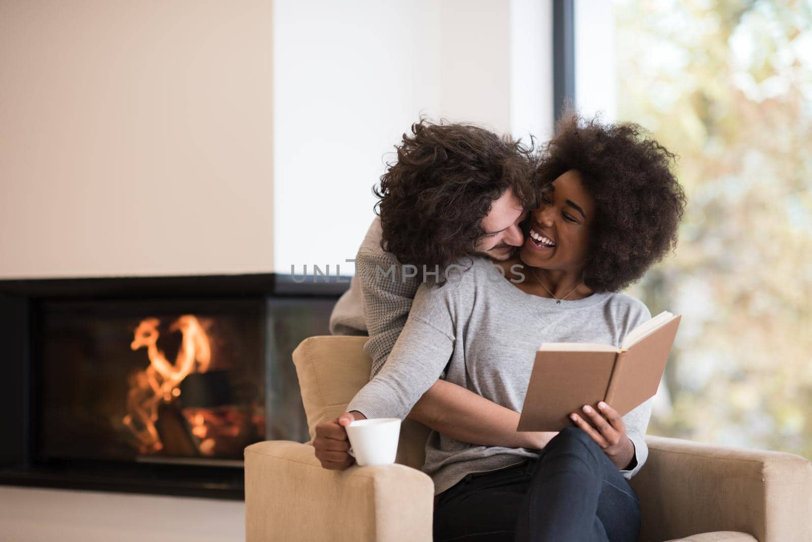 Young beautiful multiethnic couple hugging in front of fireplace at home when reading a book at autumn day