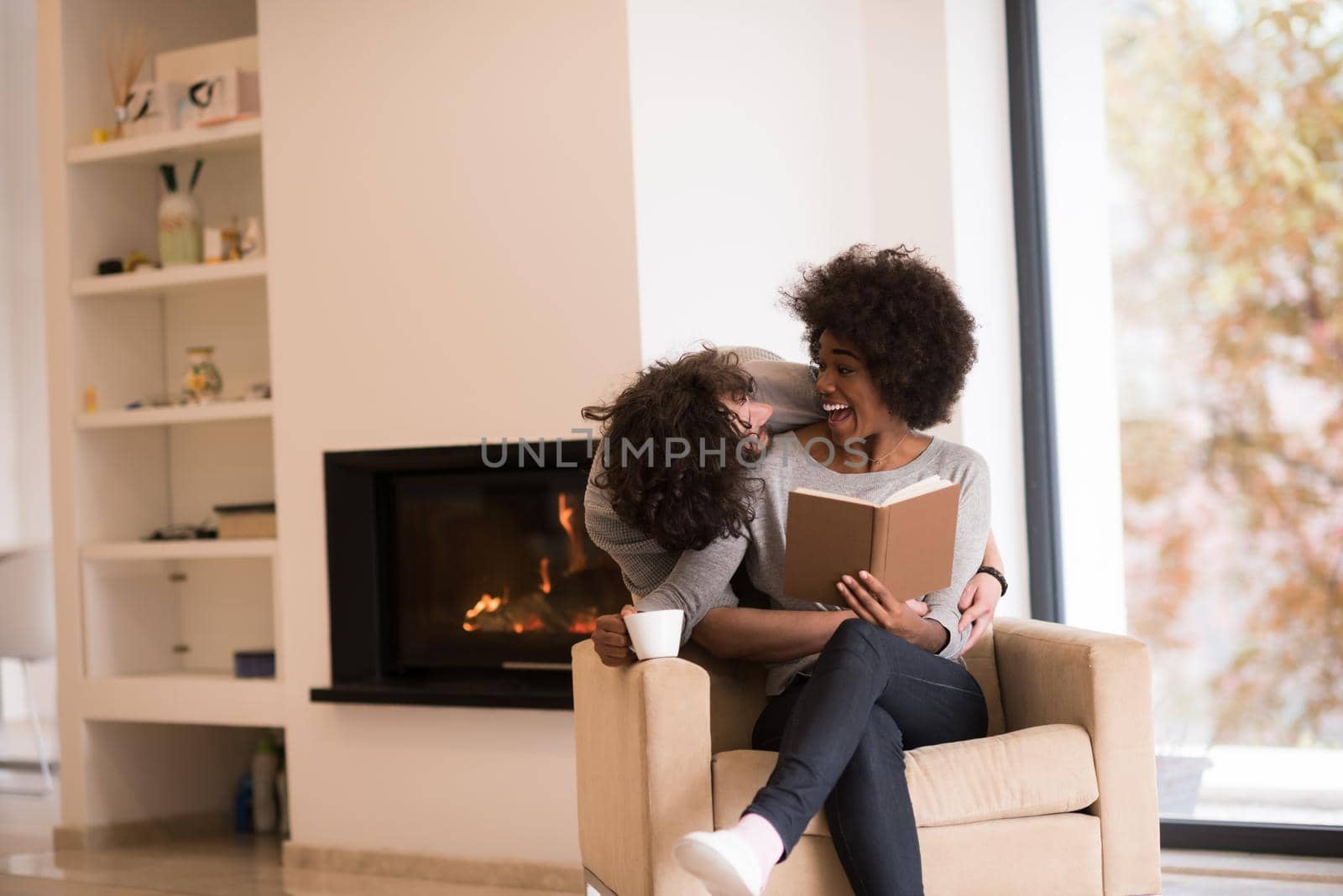 Young beautiful multiethnic couple hugging in front of fireplace at home when reading a book at autumn day