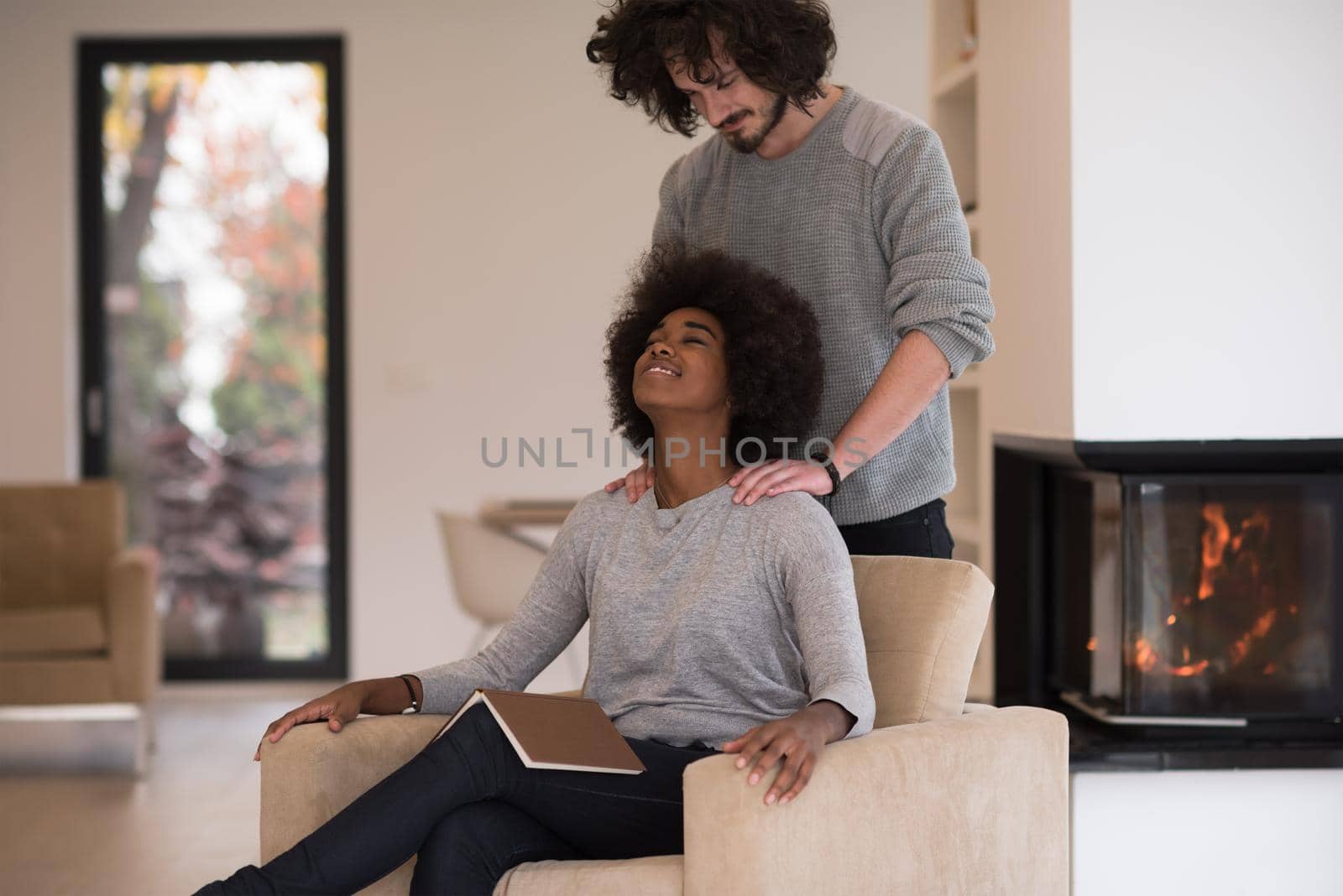 Young beautiful multiethnic couple hugging in front of fireplace at home when reading a book at autumn day