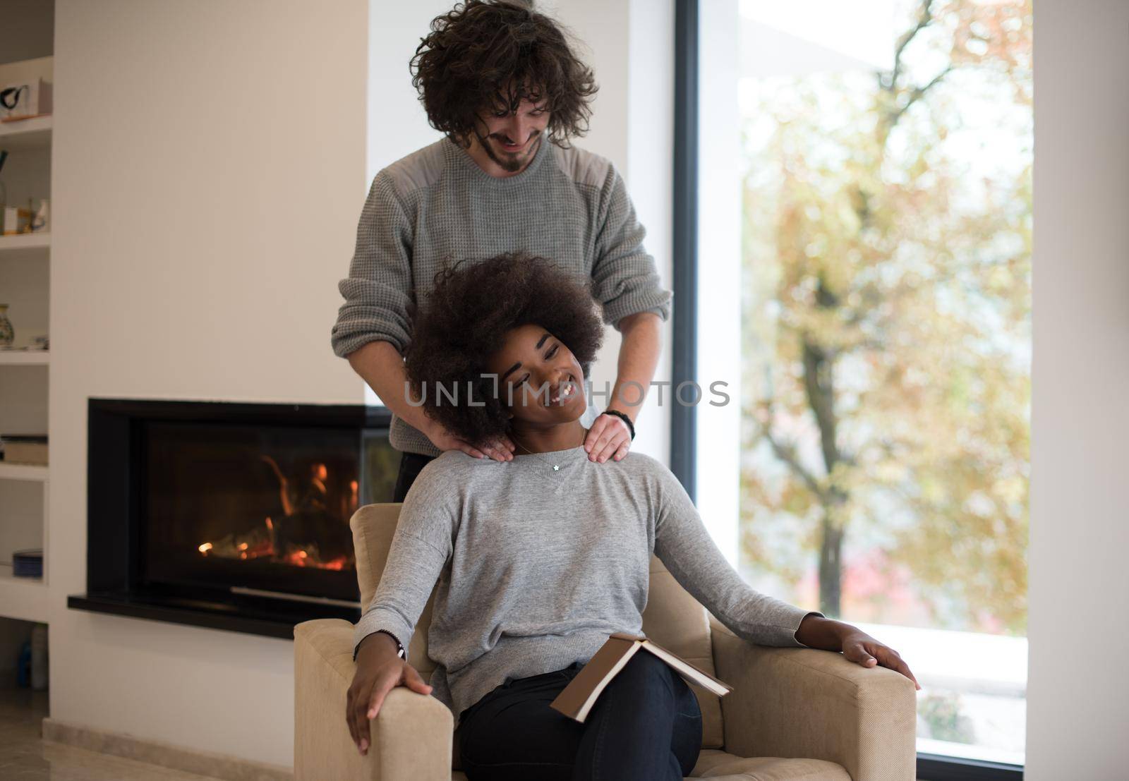 Young beautiful multiethnic couple hugging in front of fireplace at home when reading a book at autumn day