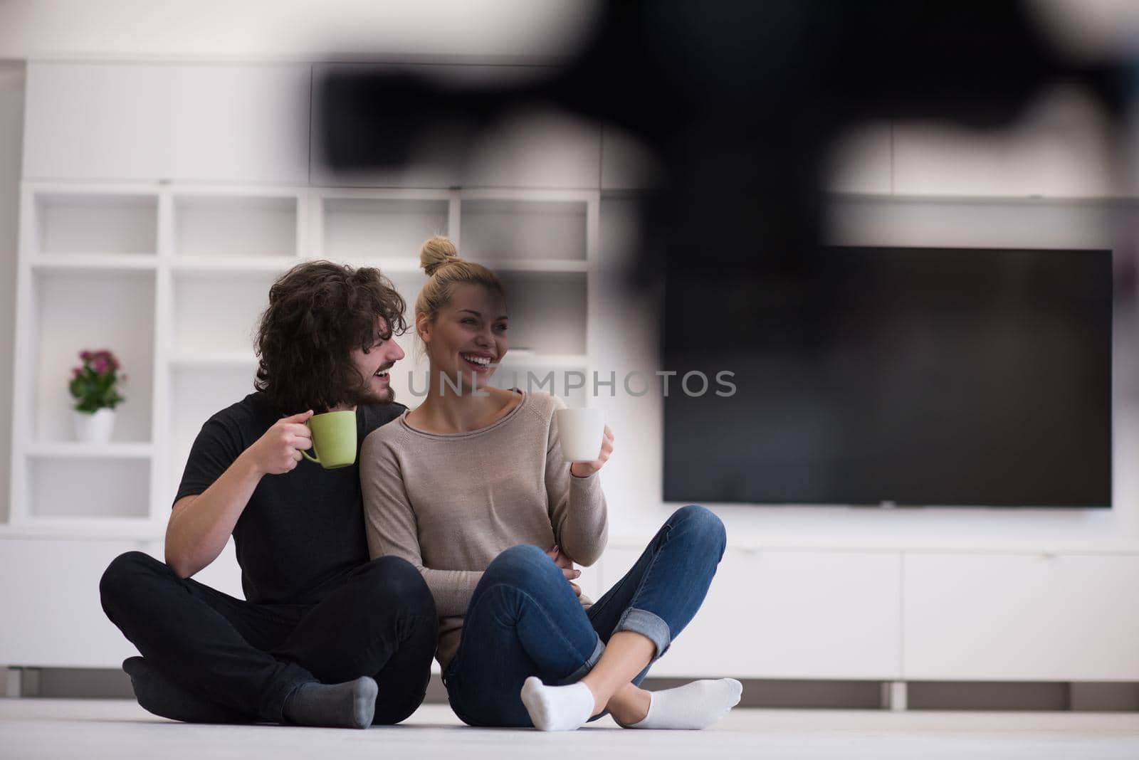 portrait of young happy beautiful couple sitting on the floor and drinking coffee in their new home