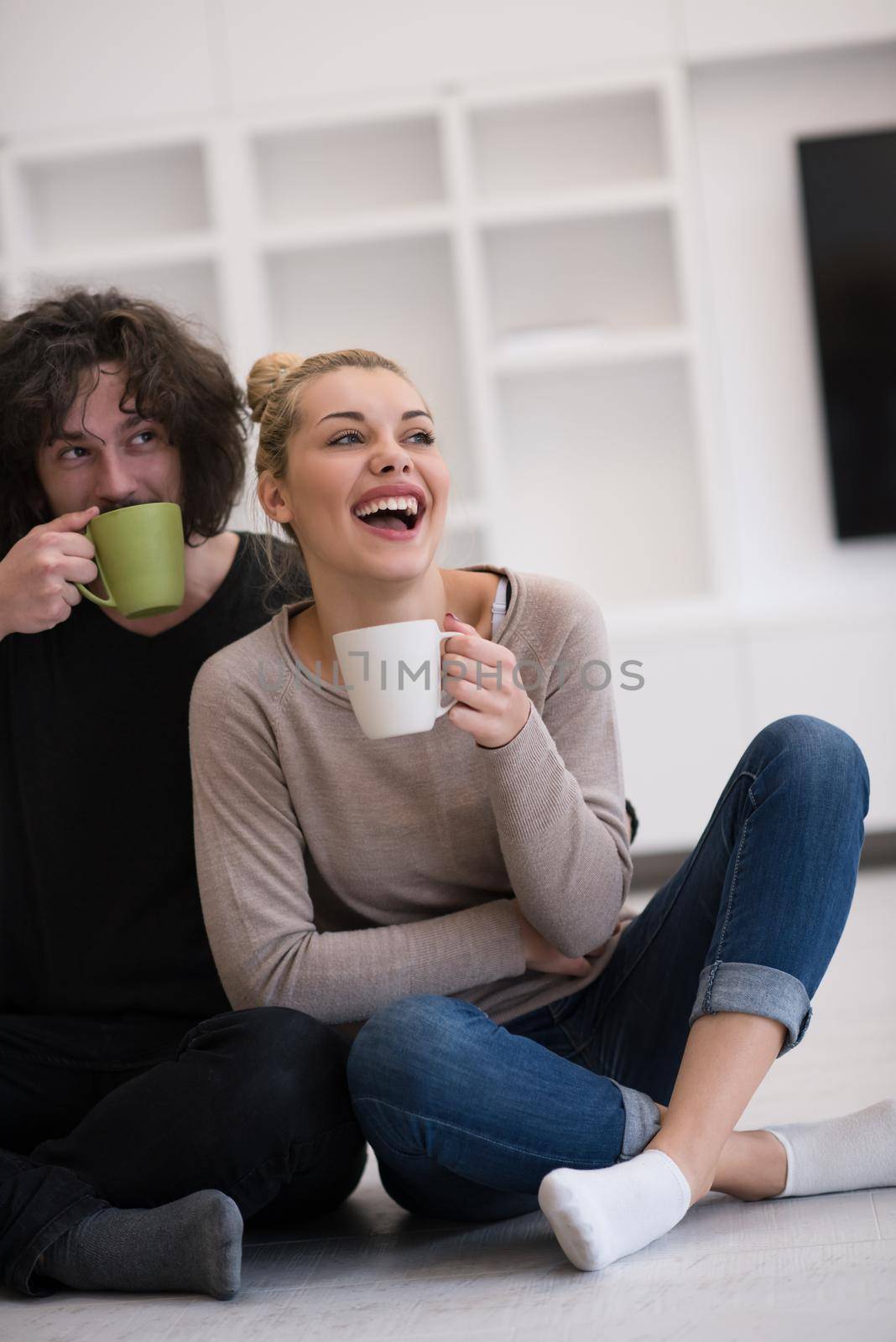 portrait of young happy beautiful couple sitting on the floor and drinking coffee in their new home