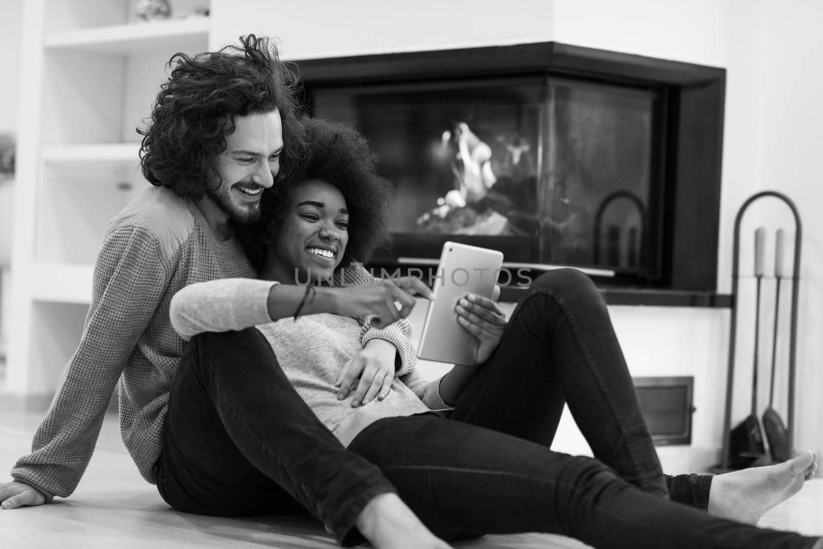 beautiful young multiethnic couple used tablet computer on the floor of their luxury home in front of fireplace autumn day