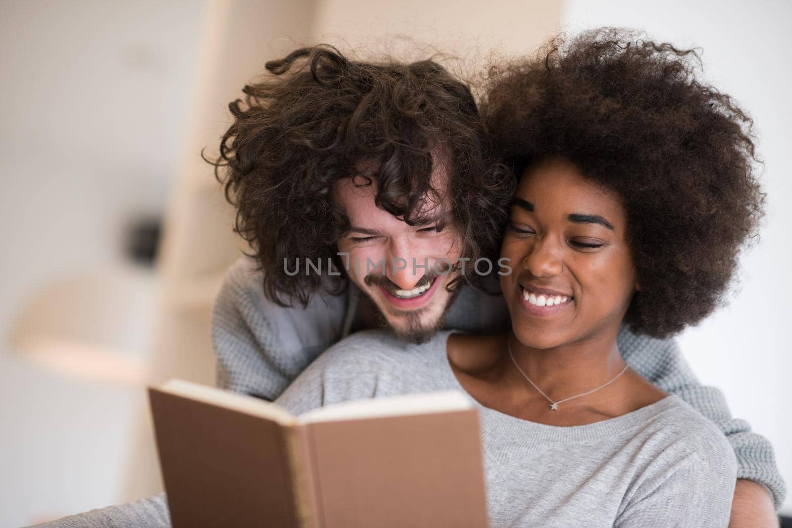 Young beautiful multiethnic couple hugging in front of fireplace at home when reading a book at autumn day