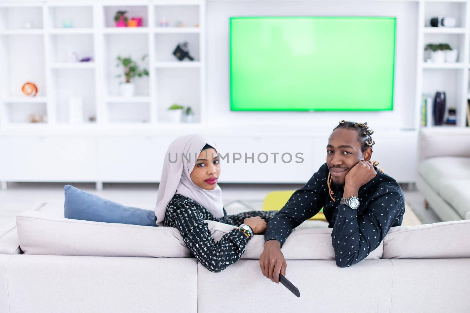 African Couple Sitting On Sofa Watching TV Together Chroma Green Screen Woman Wearing Islamic Hijab Clothes