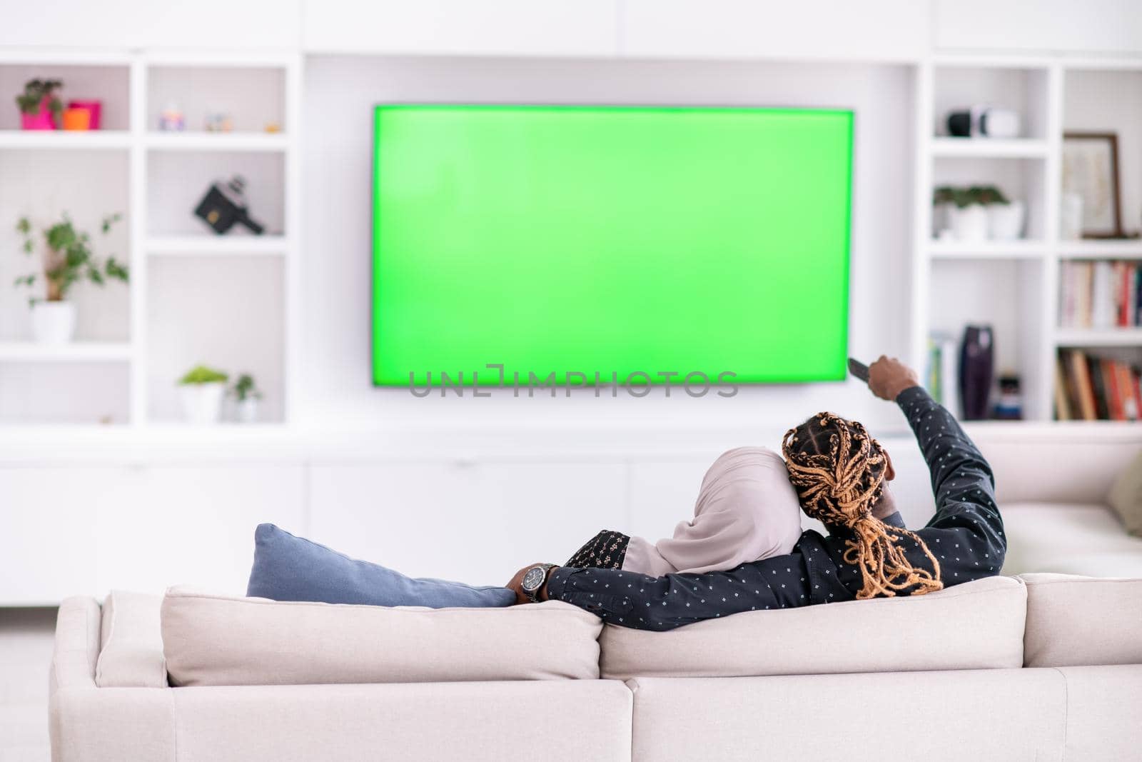 African Couple Sitting On Sofa Watching TV Together Chroma Green Screen Woman Wearing Islamic Hijab Clothes