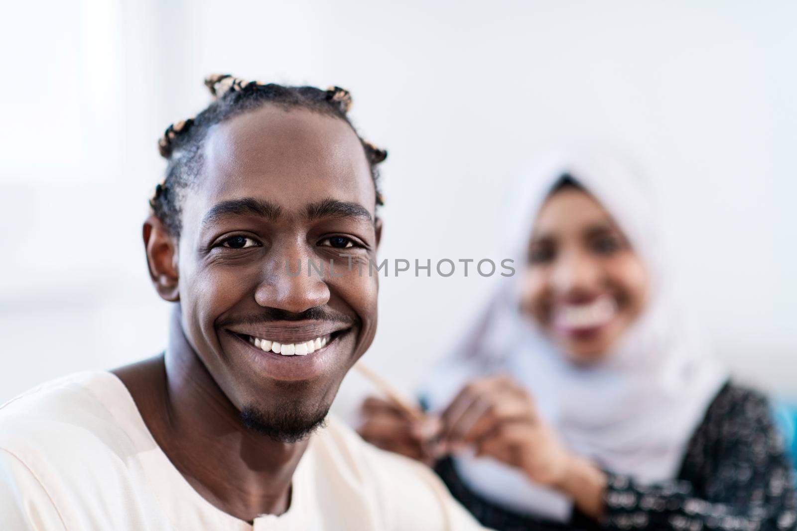 young afro modern muslim couple having romantic time at home while woman making hairstyle to husband female wearing traditional sudan islamic hijab clothes