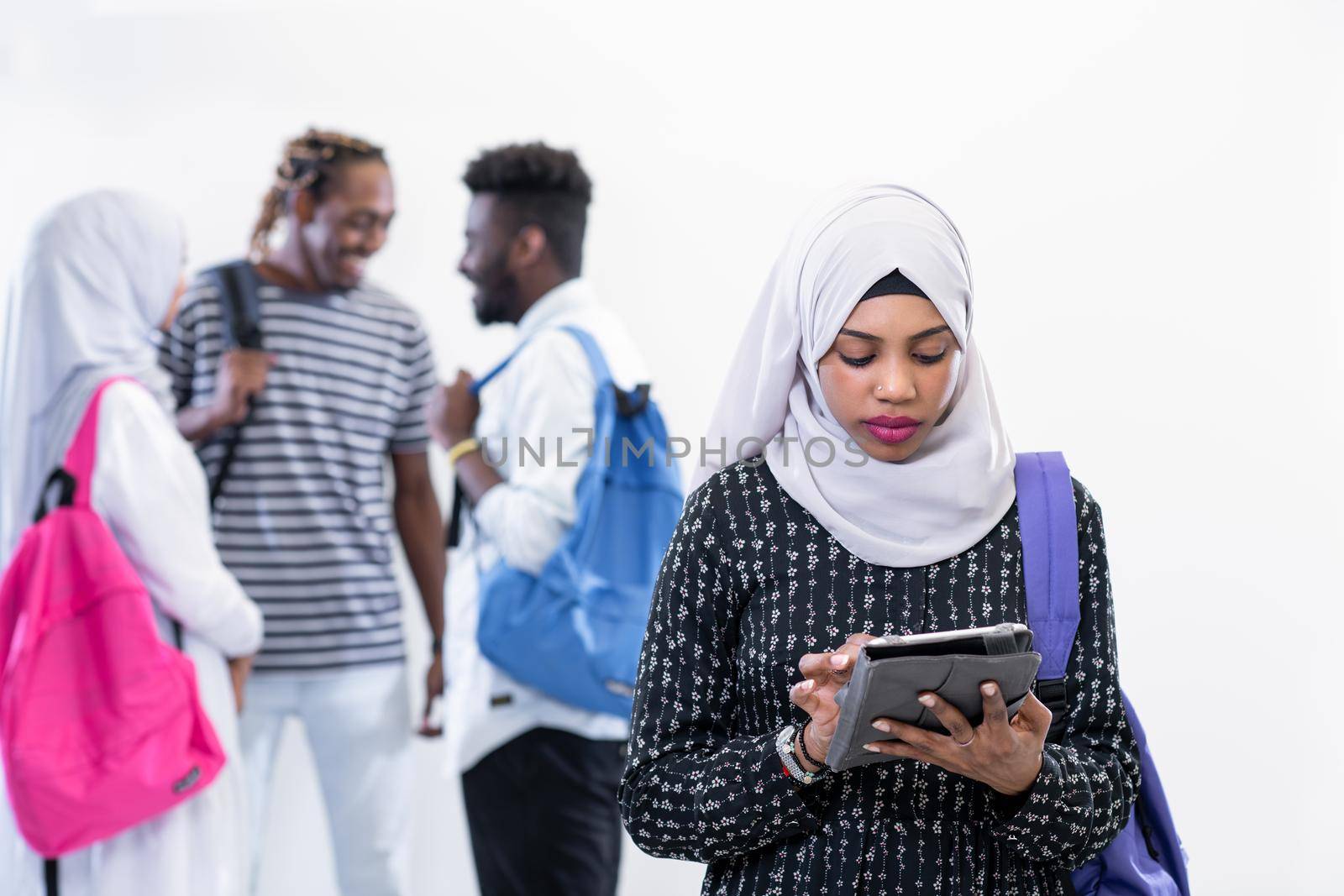 young african modern muslim female student using tablet computer with group of friends in background  wearing traditional Islamic hijab clothes