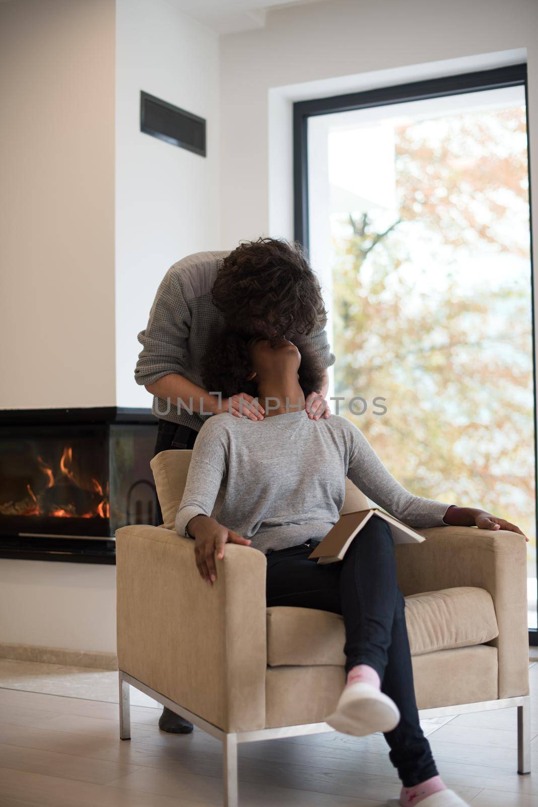 Young beautiful multiethnic couple hugging in front of fireplace at home when reading a book at autumn day