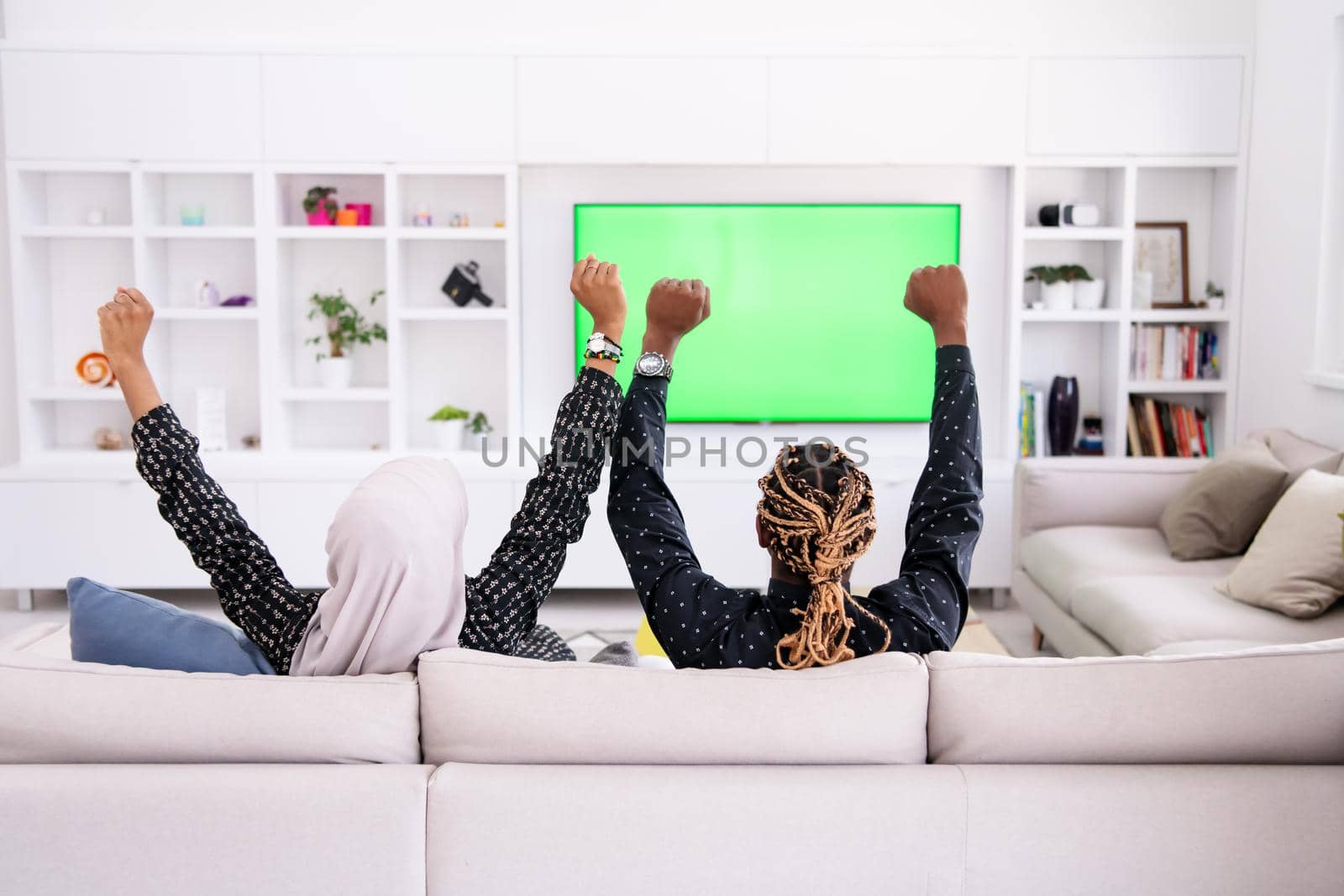 African Couple Sitting On Sofa Watching TV Together Chroma Green Screen Woman Wearing Islamic Hijab Clothes