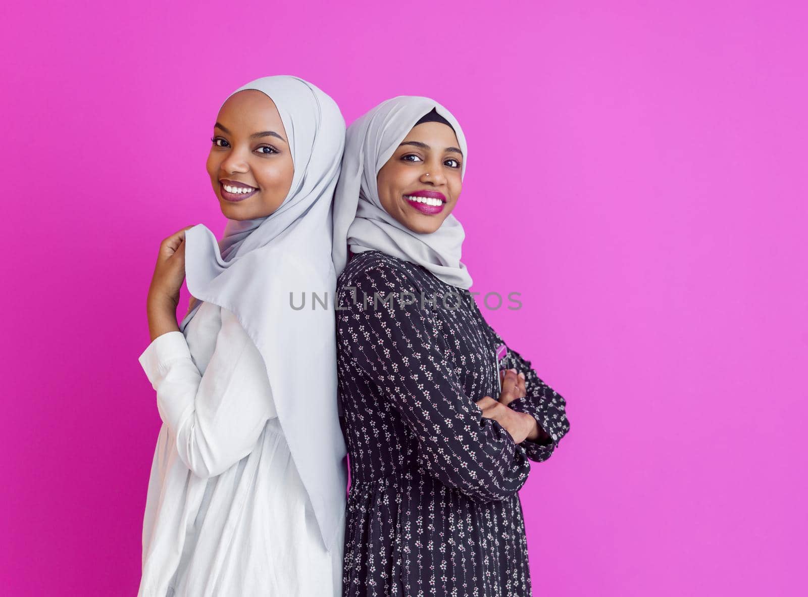 portrait of two young modern muslim afro beauty wearing traditional islamic clothes on plastic pink background