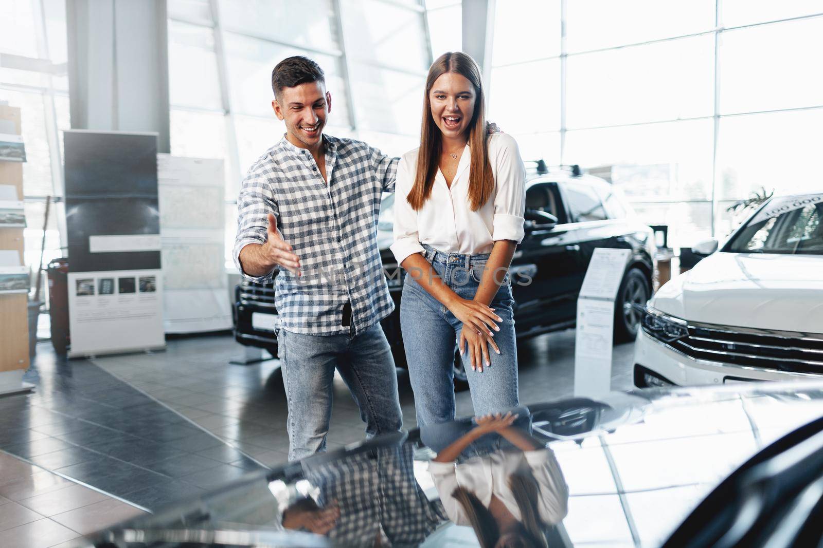 Young happy couple just bought a new car in a dealership showroom