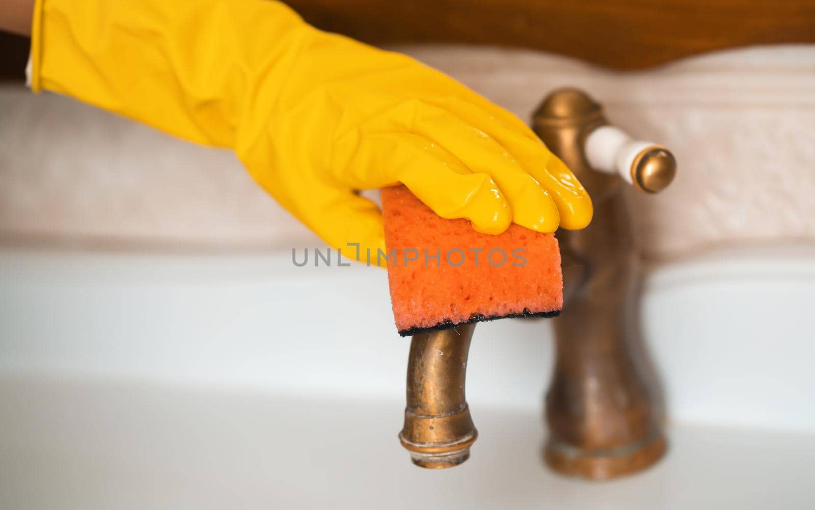 A woman in rubber gloves is cleaning the house, creating cleanliness and disinfection, wiping the faucet and wash basin in the bathroom with a sponge.