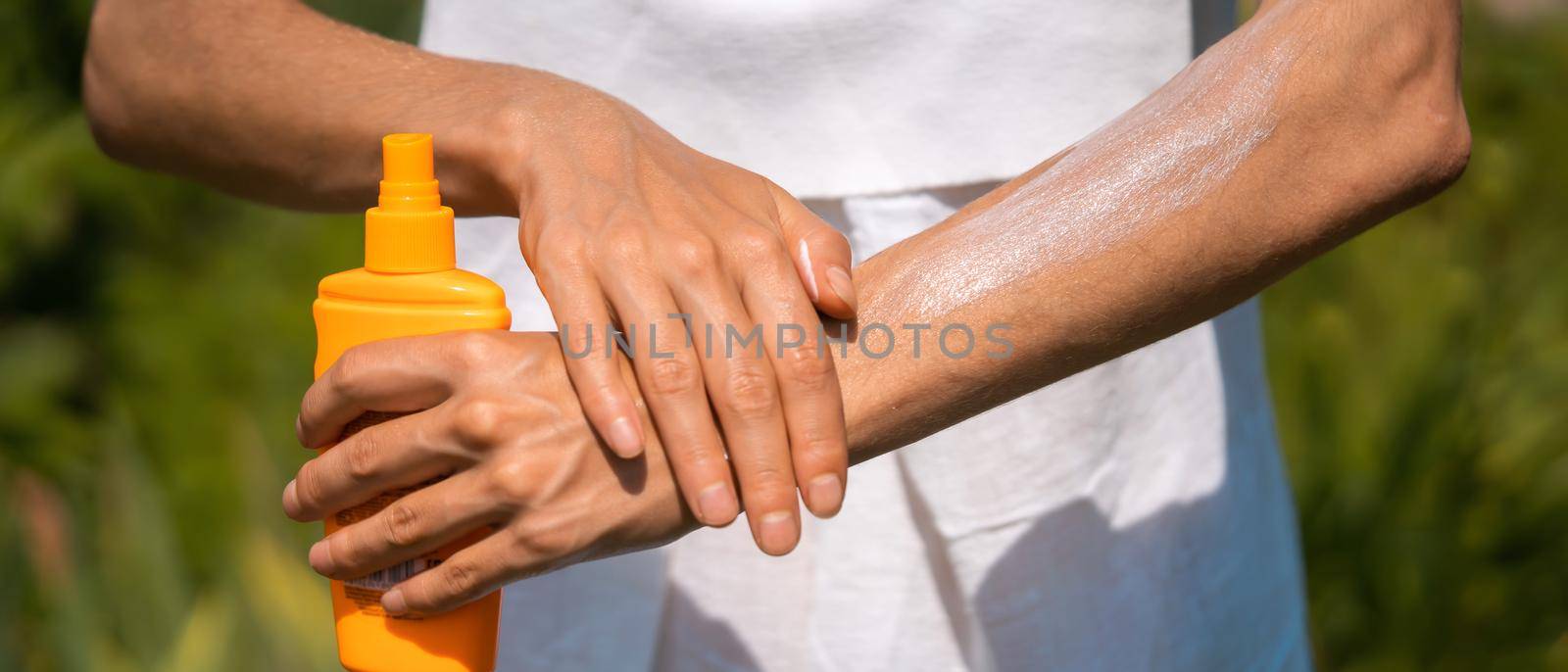 A young girl in a white summer dress applies sunscreen gel to her arms and shoulders. by africapink