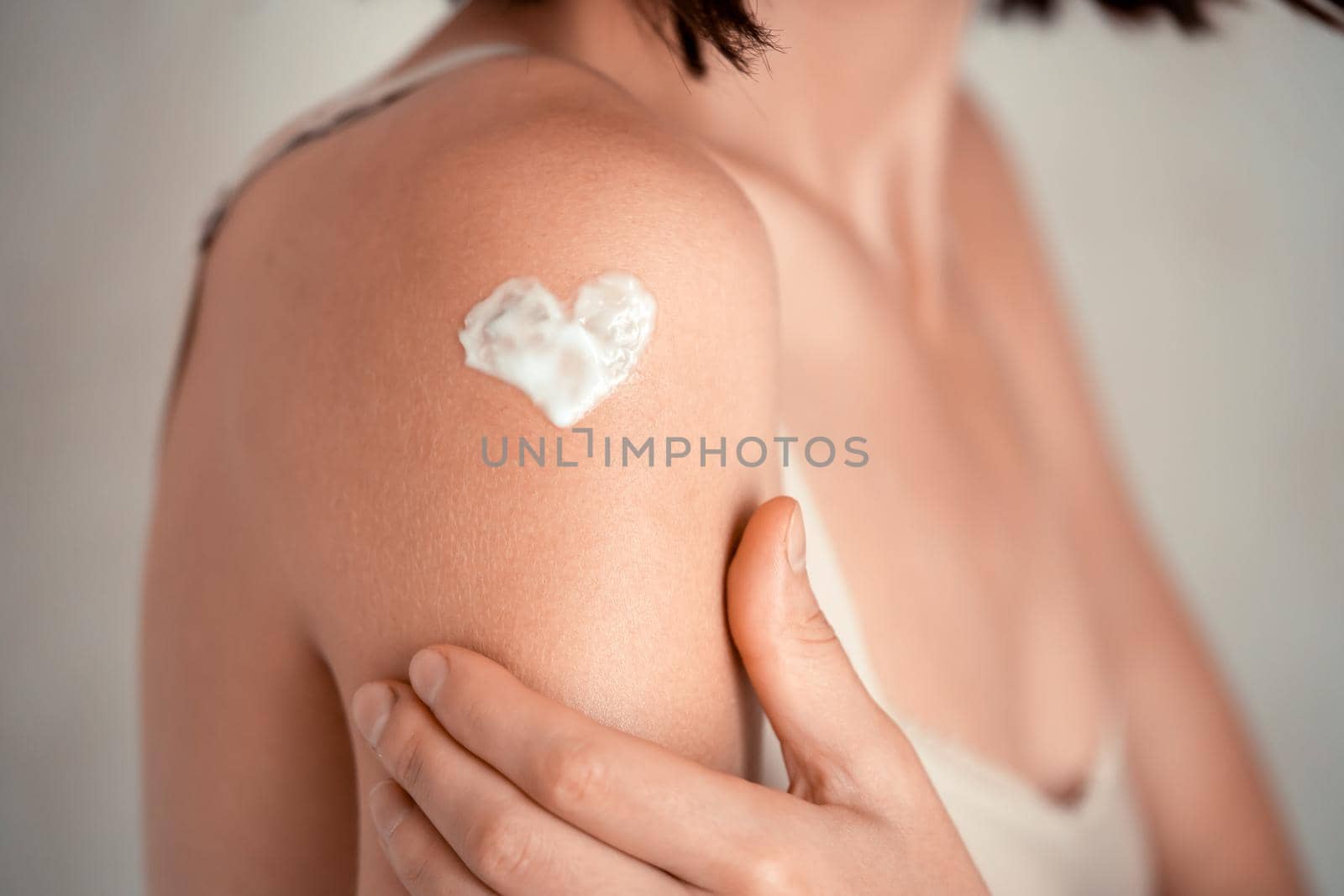 A young girl applies a moisturizer to her skin, a woman gently cares for her body, depicts a heart with a cream, taking care of herself, beauty and health.