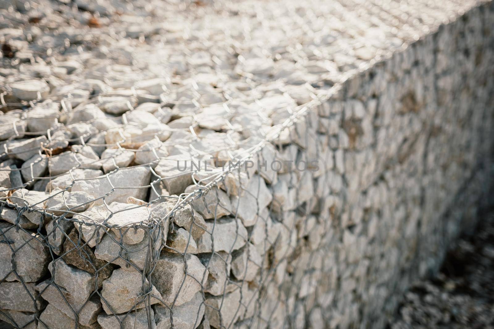 strengthening the slope with stones behind the wire. grey texture. construction. Granite stones behind a metal grate