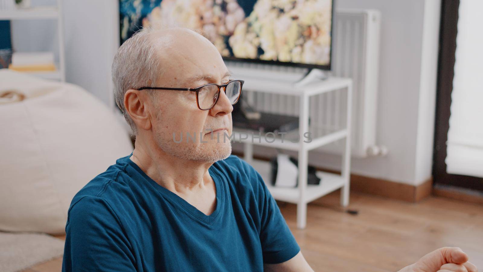 Close up of retired person relaxing with meditation activity at home. Elder man using yoga lotus position on mat to meditate and focus on wellness. Calm adult doing recreation exercise.