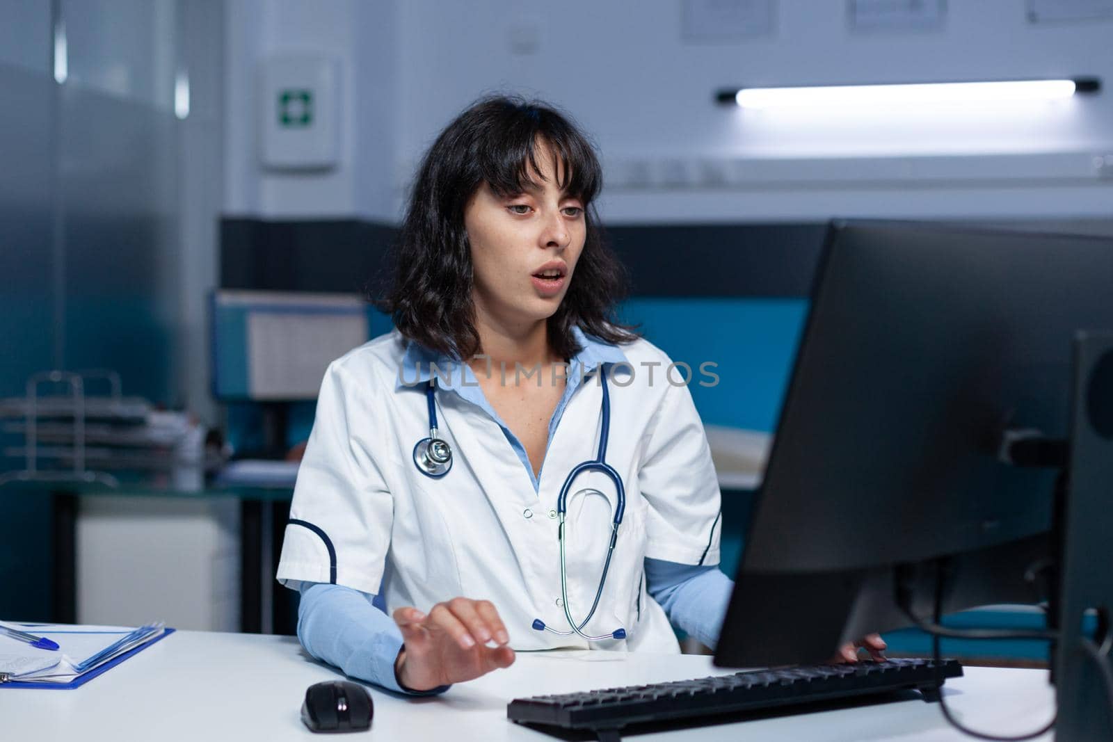 Practitioner typing on computer keyboard at office, working late at night. Woman medic with stethoscope looking at monitor screen for healthcare system and assistance after hours