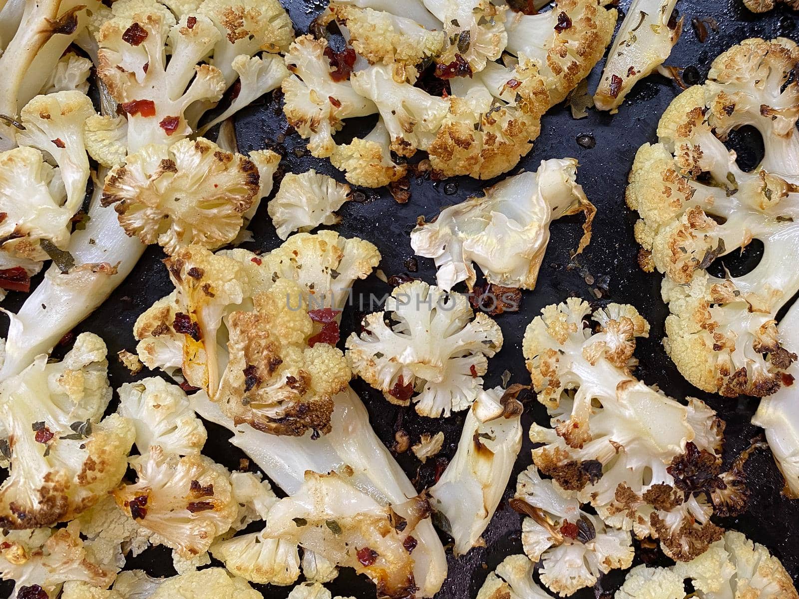 Cauliflower steaks baked with olive oil, herbs and spices on a black baking sheet background. Close-up.