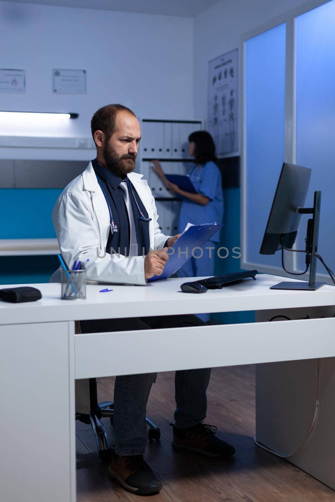 Troubled medic working with monitor and healthcare papers for consultation and examination. Doctor using computer for medical information and analysis overtime. Health practitioner