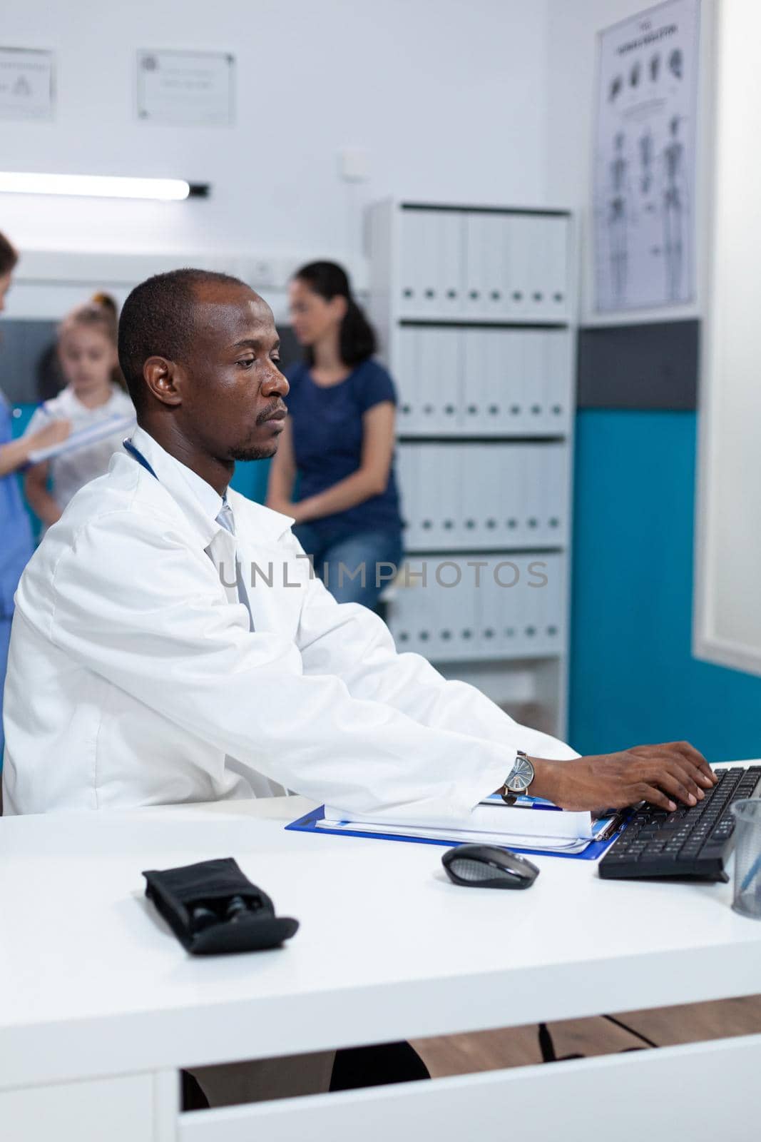 African american pediatrician doctor sitting at desk in hospital office by DCStudio