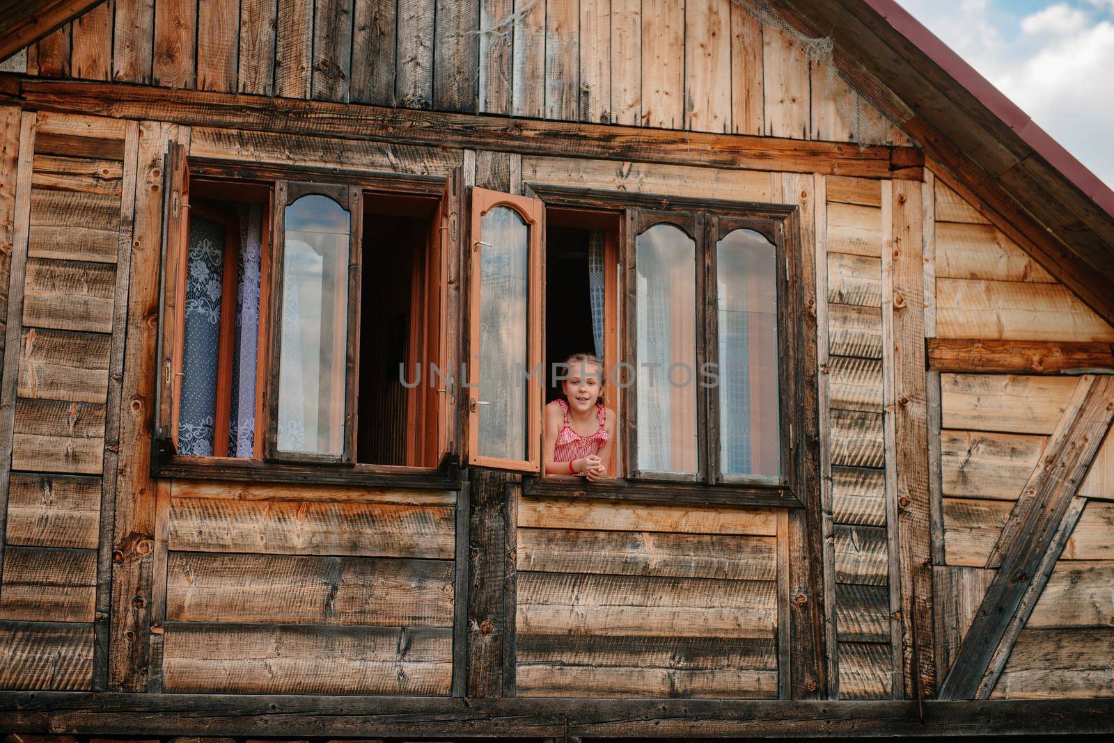 Silhouette of a young woman in the window of a wooden house in the mountains. Calm rest, alone with nature. In harmony with yourself. Meditation. Solitude in the mountains. Portrait of beautiful woman with long hair at the window frame of wooden, forest house