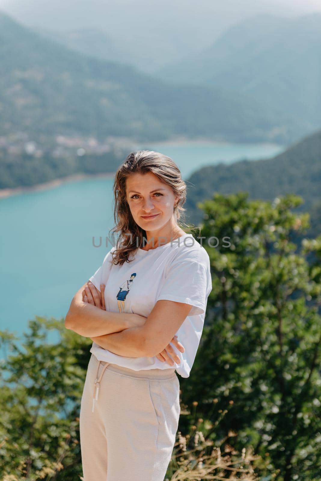 Girl tourist stands on the shore of a lake in the mountains. beautiful landscape, Piva Lake in Montenegro.. Woman is standing on the coast of Piva lake at sunset in summer. Landscape with girl, famous lake with beautiful reflection in water, trees, sky with clouds. Travel by Andrii_Ko