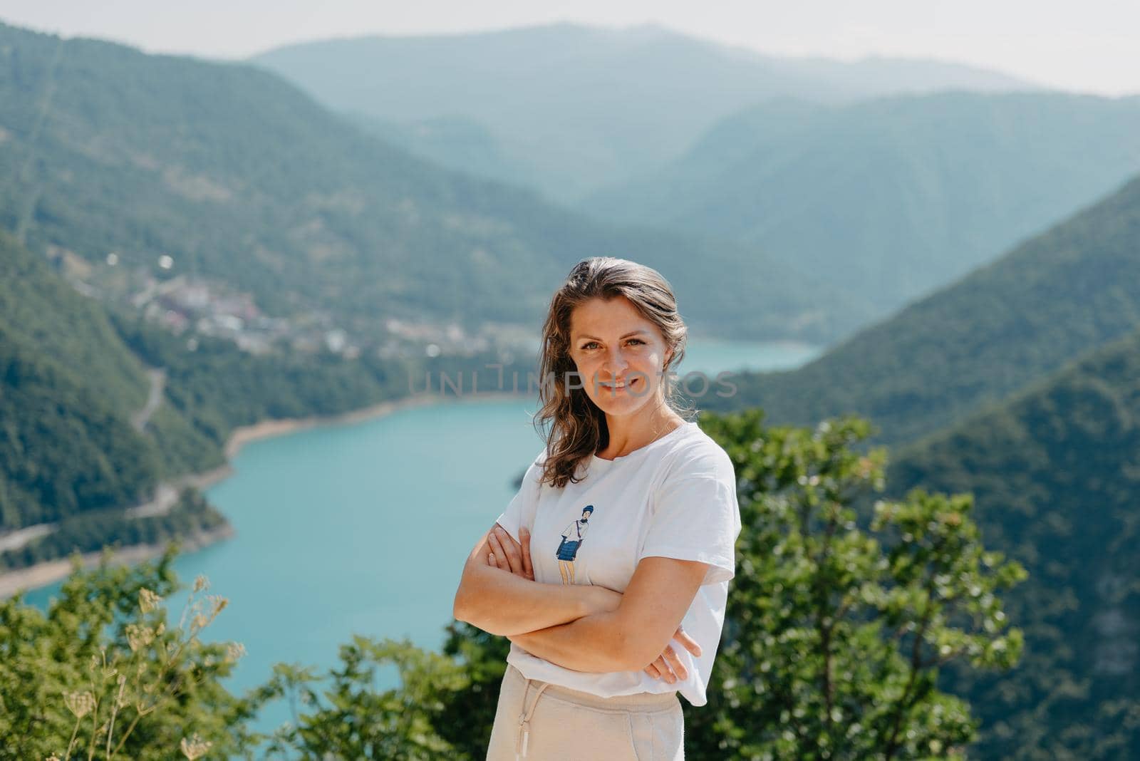 Girl tourist stands on the shore of a lake in the mountains. beautiful landscape, Piva Lake in Montenegro.. Woman is standing on the coast of Piva lake at sunset in summer. Landscape with girl, famous lake with beautiful reflection in water, trees, sky with clouds. Travel.