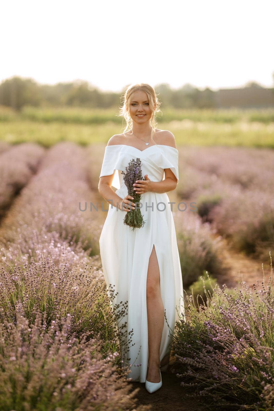 the bride in a white dress walks on the lavender field