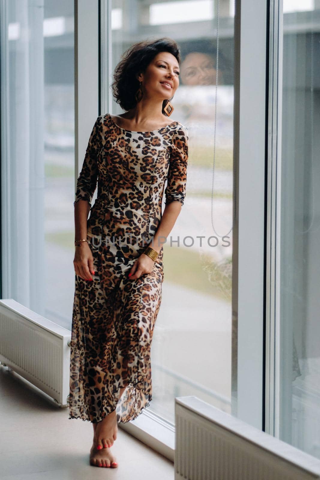 a brunette woman in a tiger dress stands near a large window.