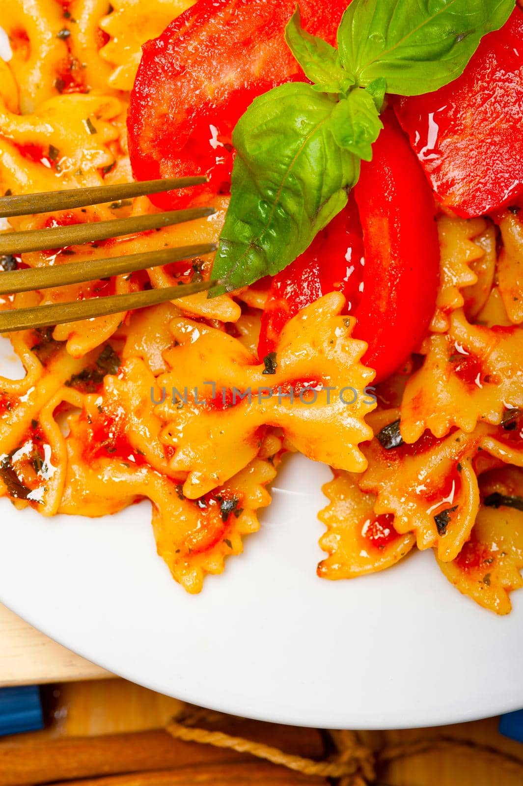 Italian pasta farfalle butterfly bow-tie with tomato basil sauce over white rustic wood table