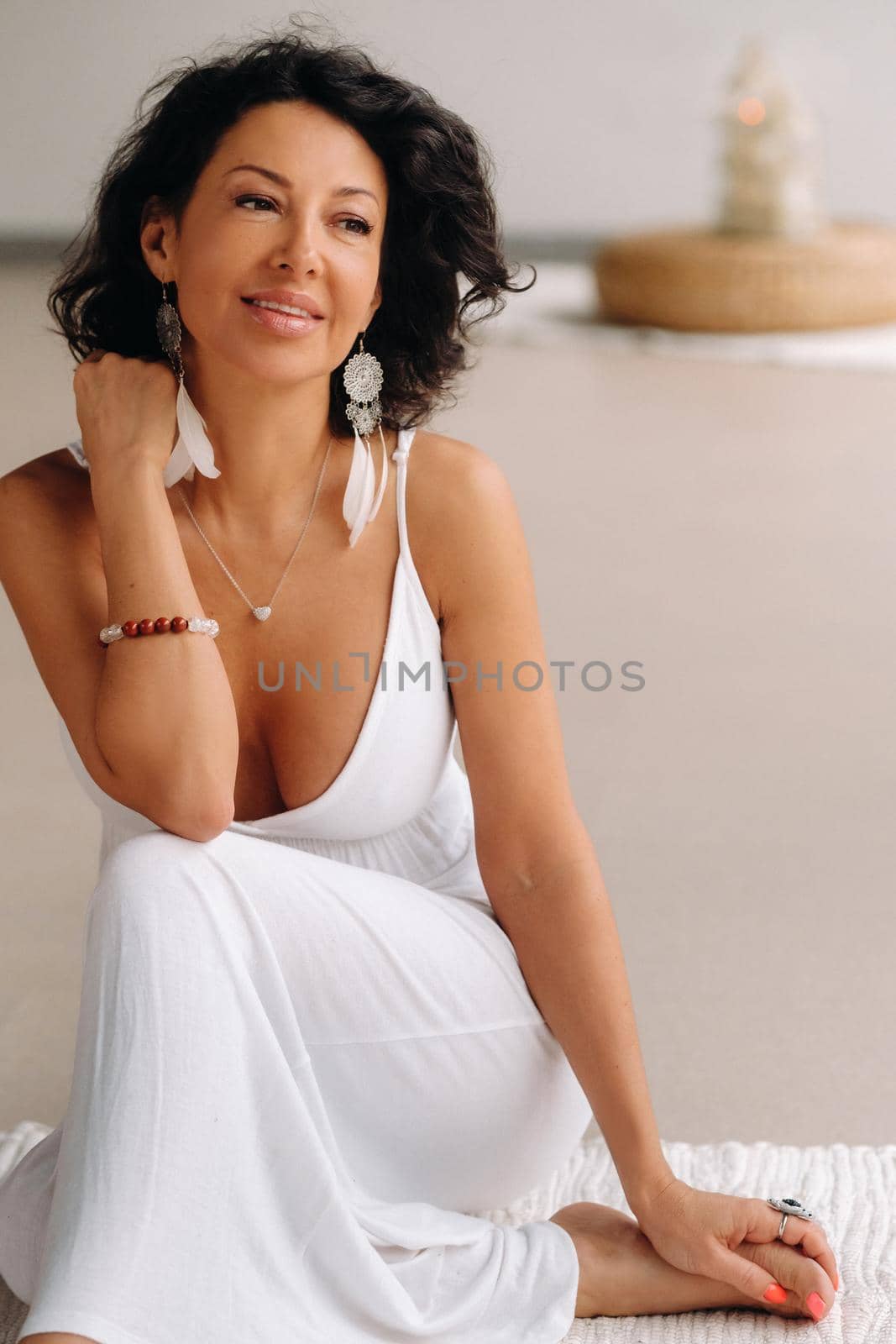 a woman in a white sundress in a bright interior is sitting on a white rug. The concept of relaxation.