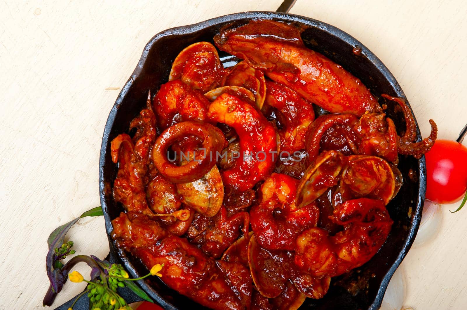 fresh seafood stew prepared on an iron skillet ove white rustic wood table 